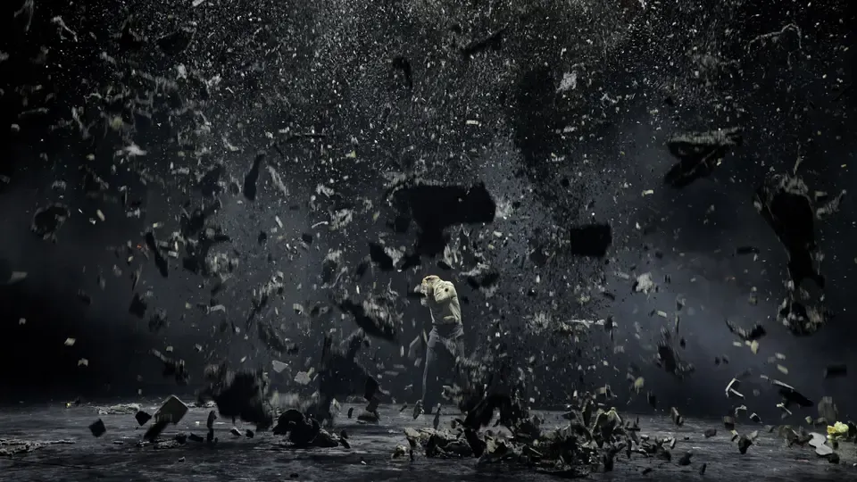 Christian Higer in der Rolle des Karl Anton Winter in „Die Flucht“. Er steht auf einer schwarzen Bühne, schwarze Asche regnet herunter.